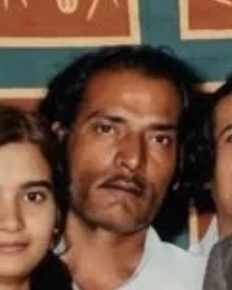 Close crop of Mohammadbhai Dekhaiya’s face: dark wavy hair and a moustache, with other faces at the edges. Colourised crop.