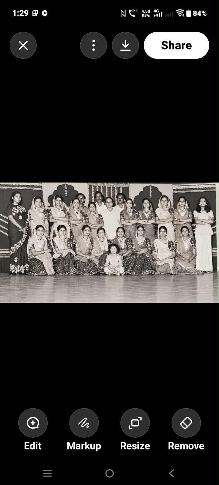 Phone screenshot of a small group photograph: a large stage group in rows, a child at the front. Black-and-white, low resolution.
